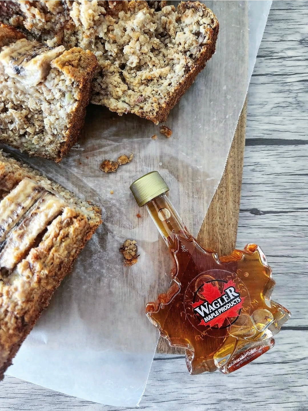 Banana bread slices with a bottle of Wagler maple syrup on a wooden surface